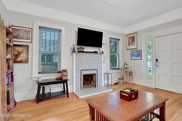 living room with a fireplace with raised hearth, a textured ceiling, wood finished floors, and baseboards