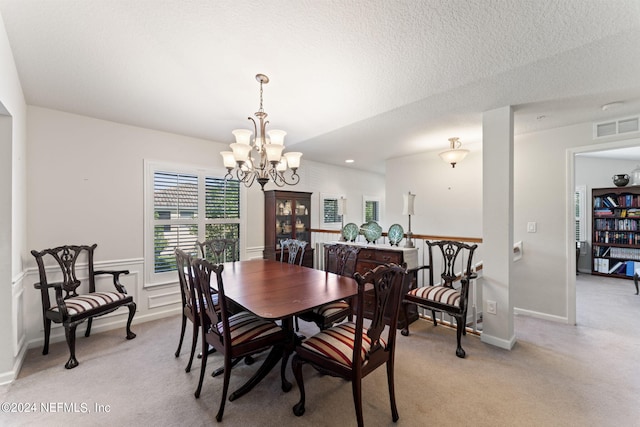 dining area featuring a textured ceiling, an inviting chandelier, visible vents, and light colored carpet