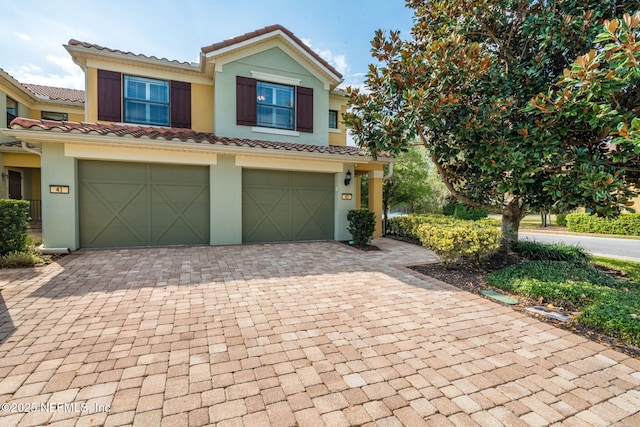 multi unit property with decorative driveway, a tiled roof, an attached garage, and stucco siding