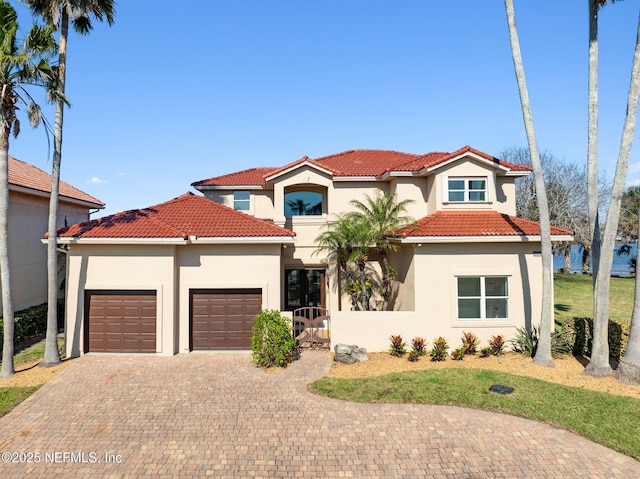 mediterranean / spanish-style home featuring an attached garage, a tile roof, decorative driveway, and stucco siding