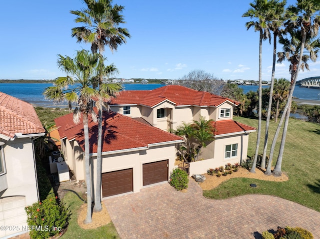 mediterranean / spanish house featuring a water view, a tiled roof, decorative driveway, stucco siding, and a front yard