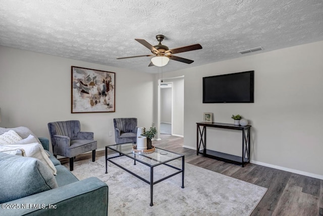 living area featuring a textured ceiling, wood finished floors, visible vents, and baseboards