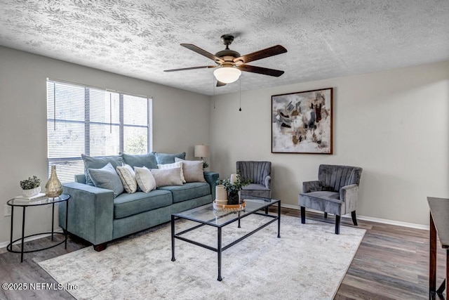 living area featuring a ceiling fan, wood finished floors, baseboards, and a textured ceiling