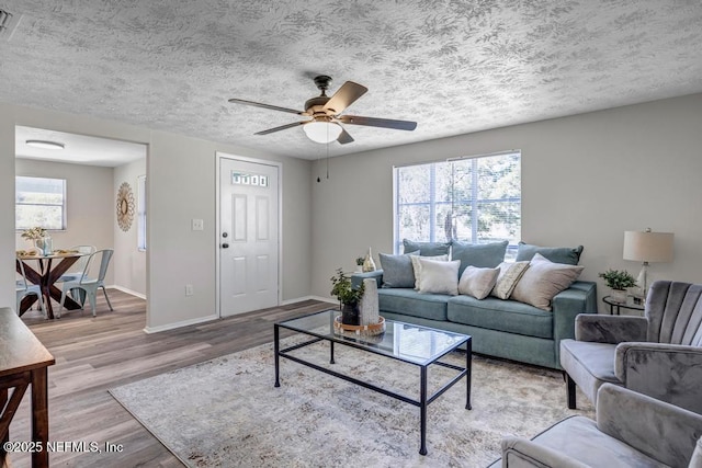 living area with ceiling fan, baseboards, a textured ceiling, and wood finished floors