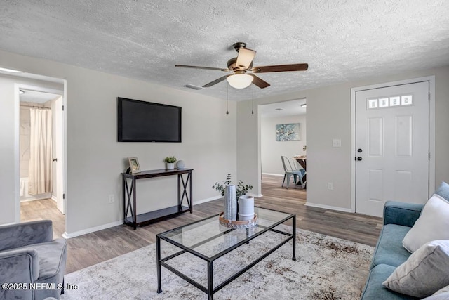 living room featuring a ceiling fan, wood finished floors, baseboards, and a textured ceiling