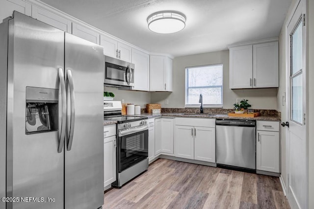 kitchen featuring dark stone counters, light wood-style flooring, stainless steel appliances, white cabinetry, and a sink