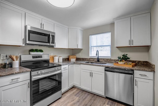 kitchen featuring light wood finished floors, dark stone countertops, appliances with stainless steel finishes, white cabinets, and a sink