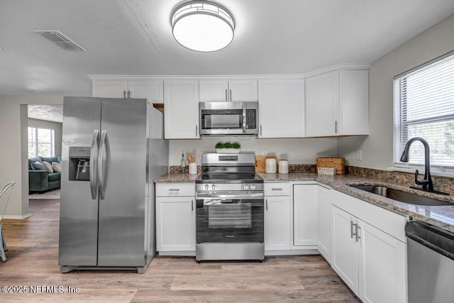 kitchen featuring visible vents, light stone countertops, stainless steel appliances, white cabinetry, and a sink