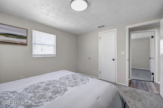 bedroom with visible vents, carpet floors, a textured ceiling, and baseboards