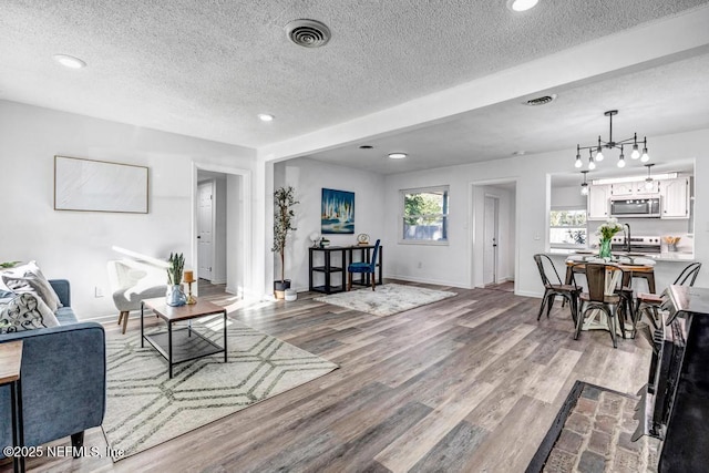 living room featuring a textured ceiling, a notable chandelier, wood finished floors, visible vents, and baseboards