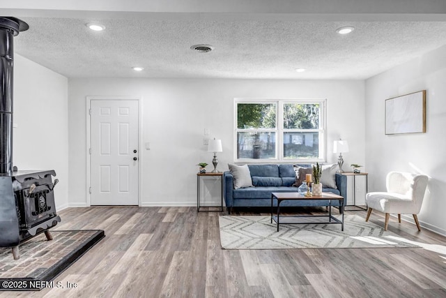 living area with recessed lighting, visible vents, light wood-style floors, a wood stove, and a textured ceiling