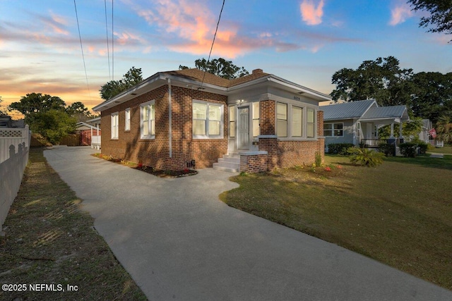 bungalow featuring fence, a front lawn, and brick siding