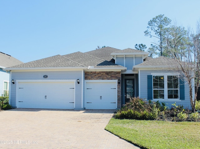 view of front of house featuring an attached garage, a front lawn, decorative driveway, and roof with shingles