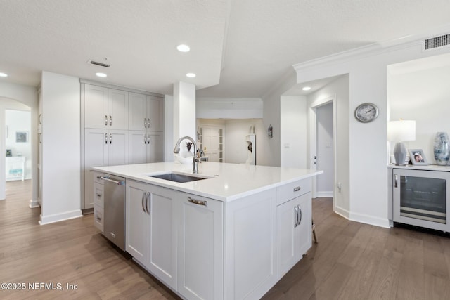 kitchen with beverage cooler, an island with sink, a sink, light countertops, and stainless steel dishwasher