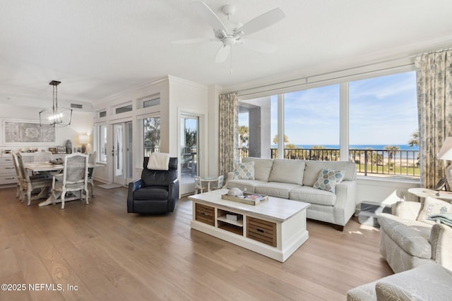 living room featuring ceiling fan with notable chandelier, a water view, visible vents, light wood-type flooring, and crown molding