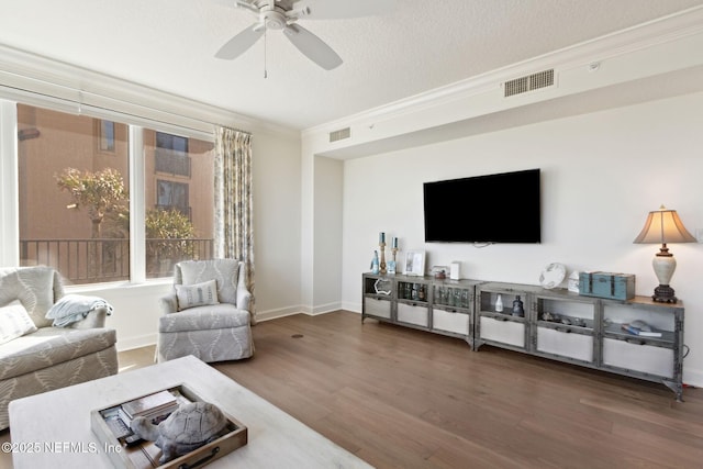 living area with a textured ceiling, visible vents, dark wood-style flooring, and ornamental molding