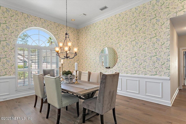 dining space featuring a wainscoted wall, dark wood finished floors, visible vents, ornamental molding, and wallpapered walls