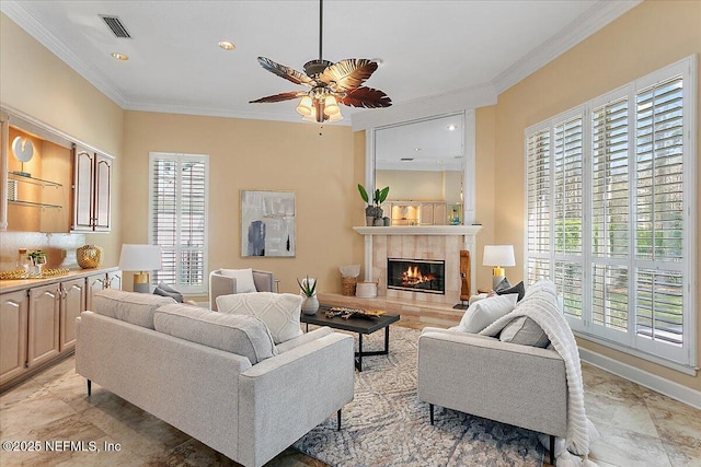 living room featuring baseboards, visible vents, a ceiling fan, a tile fireplace, and crown molding