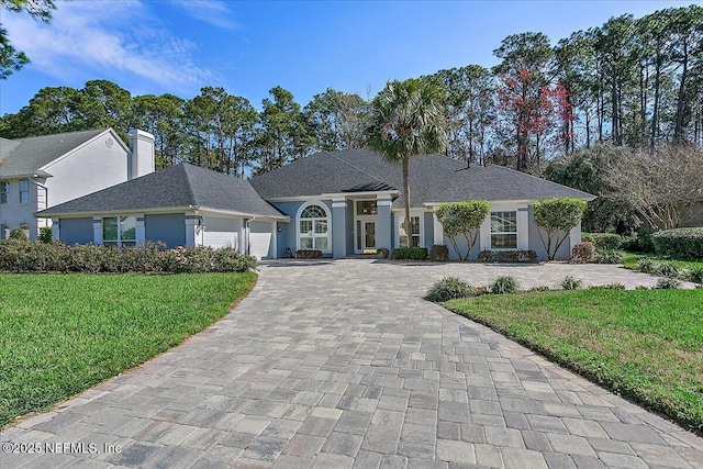 view of front facade with a garage, decorative driveway, a front lawn, and stucco siding