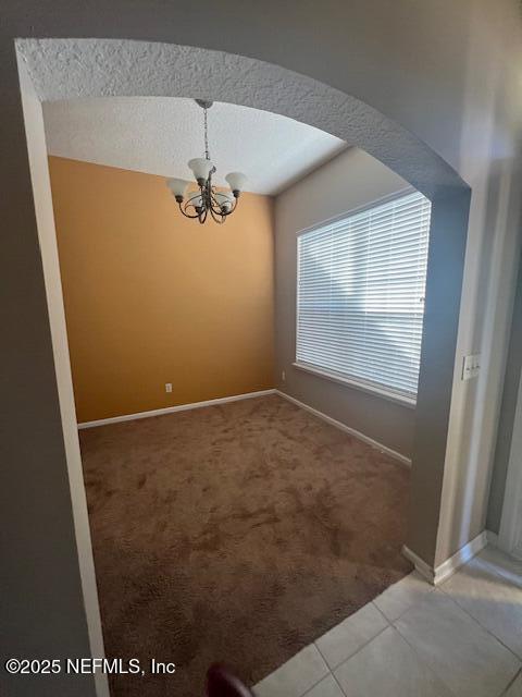 unfurnished dining area featuring baseboards, an inviting chandelier, carpet, tile patterned flooring, and a textured ceiling