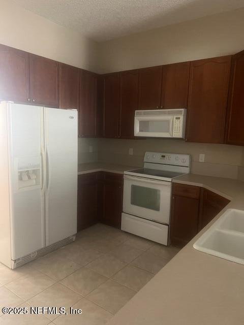 kitchen with a textured ceiling, light countertops, white appliances, and light tile patterned floors