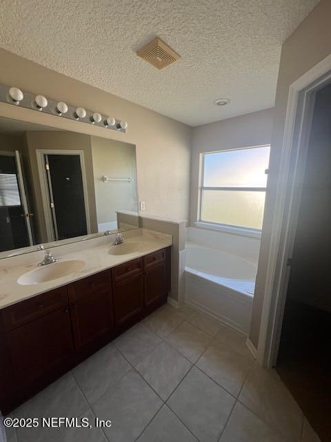 full bath with a textured ceiling, a sink, a bath, tile patterned floors, and double vanity