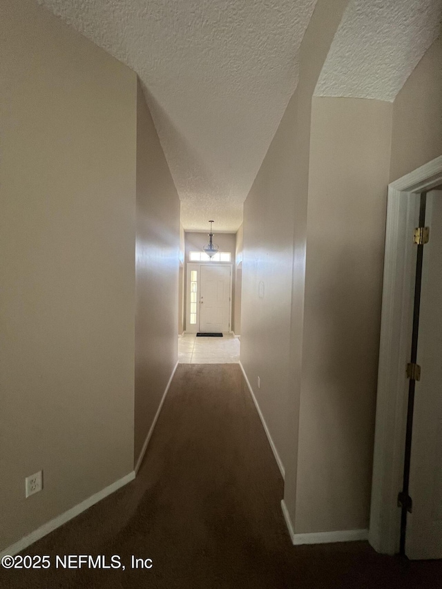 hallway featuring carpet floors, baseboards, and a textured ceiling