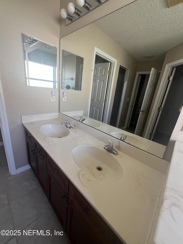 full bathroom with a textured ceiling, double vanity, a sink, and tile patterned floors