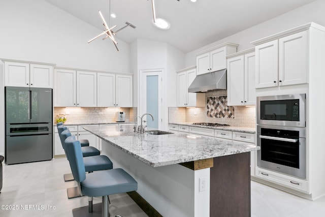 kitchen featuring an island with sink, appliances with stainless steel finishes, a kitchen breakfast bar, under cabinet range hood, and a sink