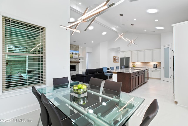 dining area with high vaulted ceiling, recessed lighting, a fireplace, and a notable chandelier