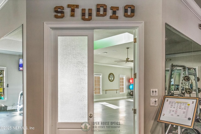 doorway featuring crown molding, a ceiling fan, wood finished floors, plenty of natural light, and baseboards