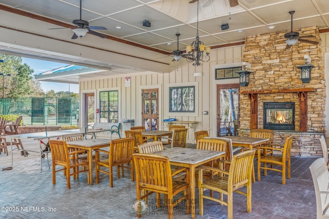 dining space featuring ceiling fan with notable chandelier, a stone fireplace, and brick floor