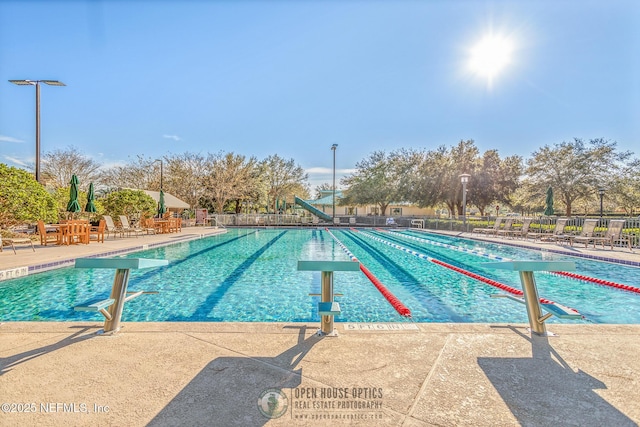 community pool with a patio area, fence, and a water slide