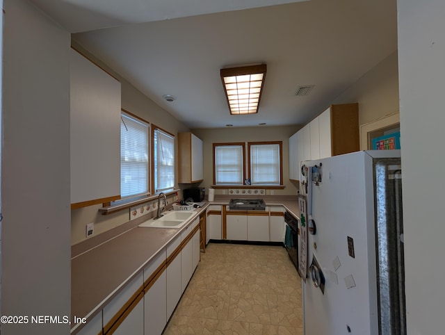 kitchen with a sink, visible vents, white cabinetry, light countertops, and freestanding refrigerator