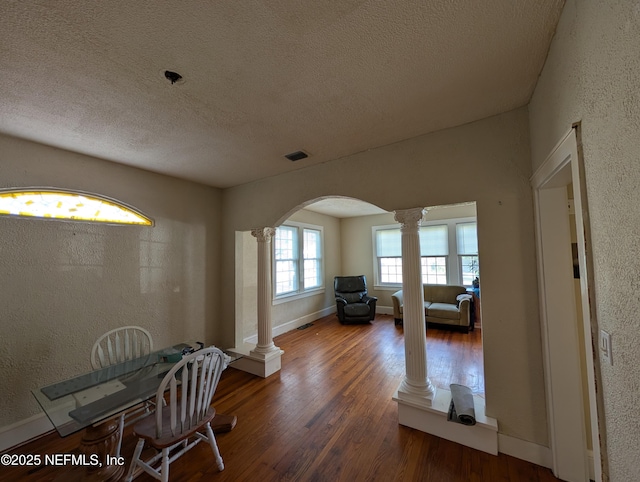 interior space featuring dark wood-style floors, arched walkways, visible vents, and decorative columns