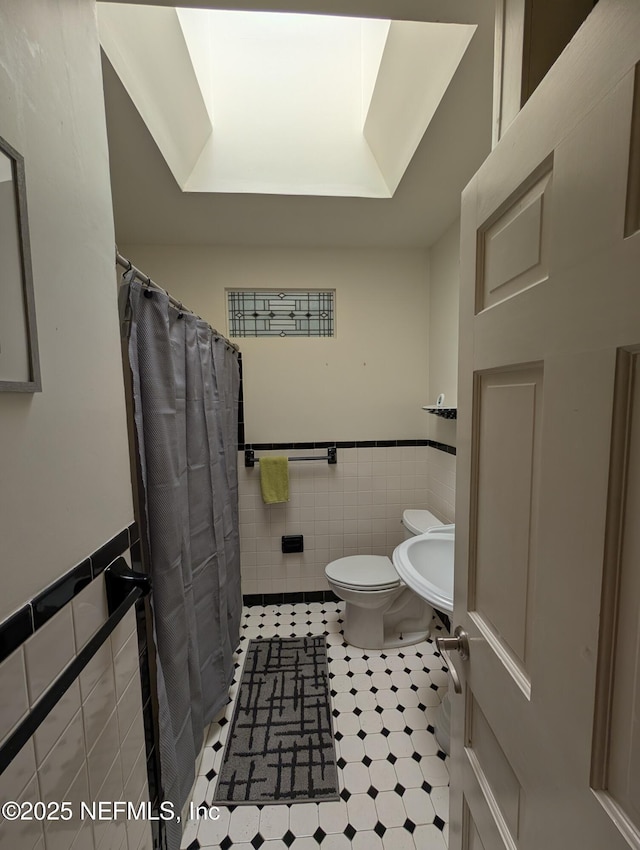 bathroom with curtained shower, toilet, a wainscoted wall, a sink, and tile walls