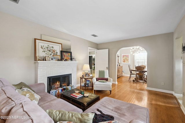 living area featuring visible vents, an inviting chandelier, a brick fireplace, wood finished floors, and baseboards