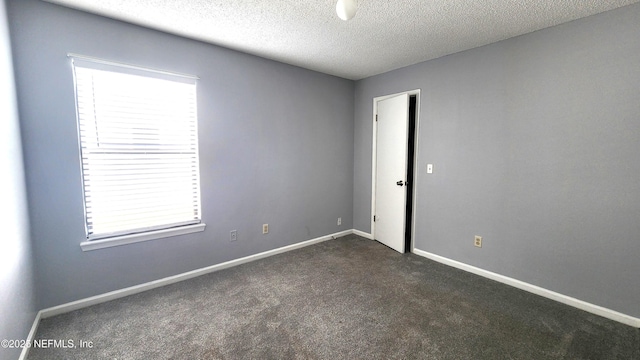 empty room featuring a textured ceiling, dark colored carpet, and baseboards