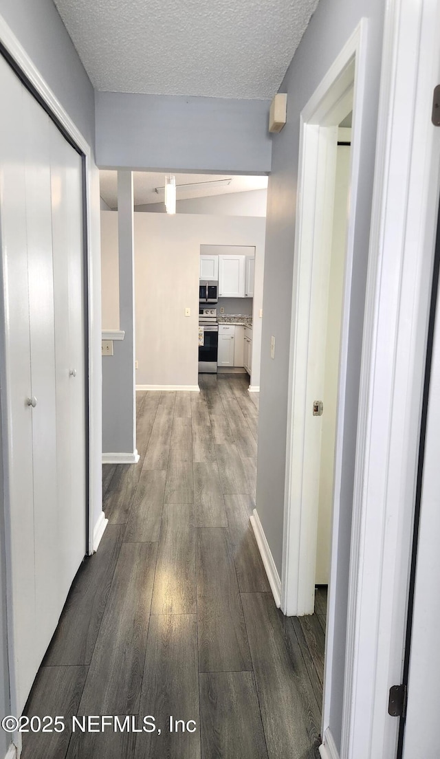 hall with a textured ceiling, baseboards, and wood finished floors