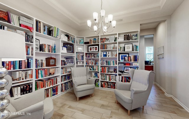 sitting room featuring a chandelier, a tray ceiling, crown molding, and wall of books