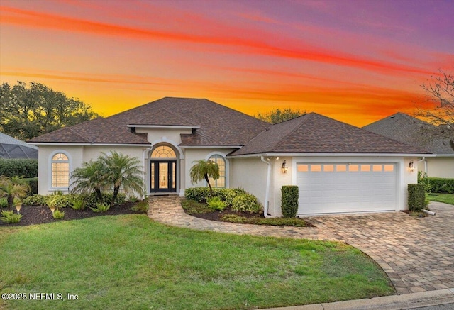 view of front of house featuring a garage, a lawn, decorative driveway, french doors, and stucco siding