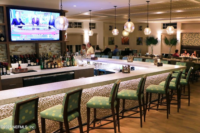 bar featuring hanging light fixtures, light wood-type flooring, and a community bar