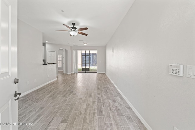 unfurnished living room with light wood-type flooring, arched walkways, ceiling fan, and baseboards