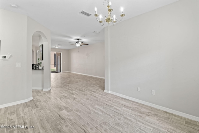 spare room with arched walkways, ceiling fan with notable chandelier, visible vents, baseboards, and light wood finished floors