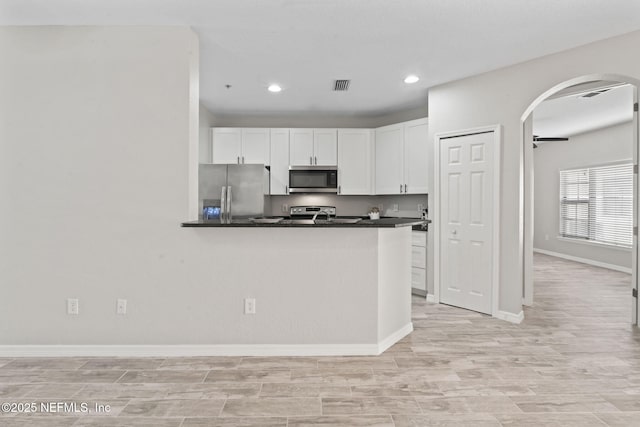 kitchen featuring visible vents, arched walkways, dark countertops, appliances with stainless steel finishes, and white cabinetry