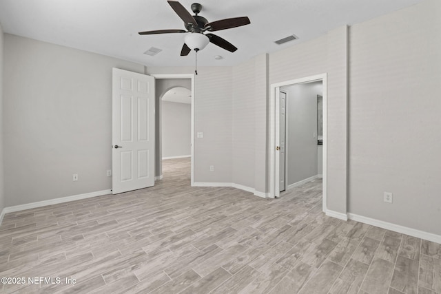 unfurnished room featuring arched walkways, visible vents, light wood-style flooring, a ceiling fan, and baseboards