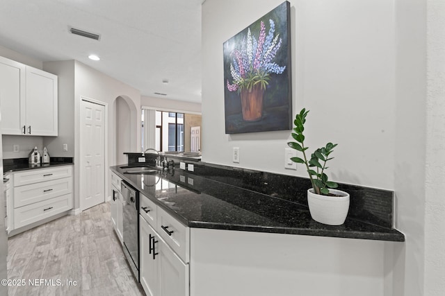 kitchen featuring visible vents, arched walkways, dark stone countertops, white cabinetry, and a sink