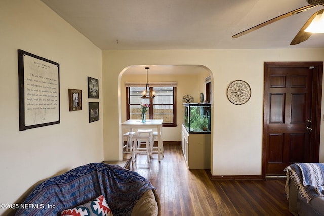 interior space with a ceiling fan, baseboards, arched walkways, and dark wood-style flooring