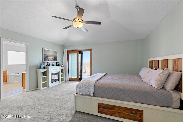 carpeted bedroom with lofted ceiling, a glass covered fireplace, ceiling fan, a textured ceiling, and access to outside