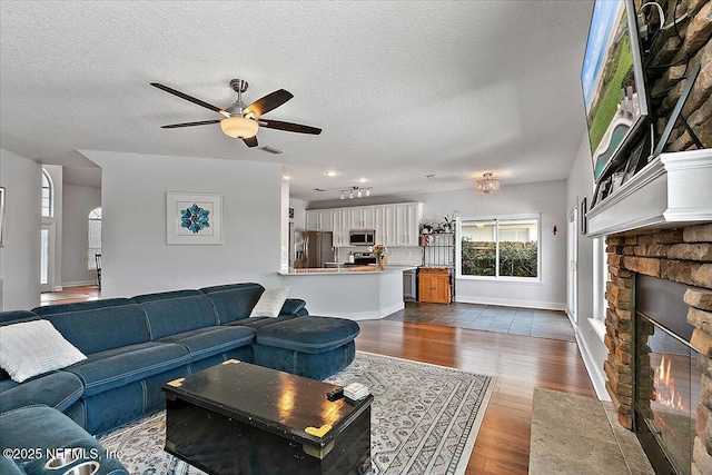 living area featuring a fireplace, dark wood-type flooring, a ceiling fan, a textured ceiling, and baseboards